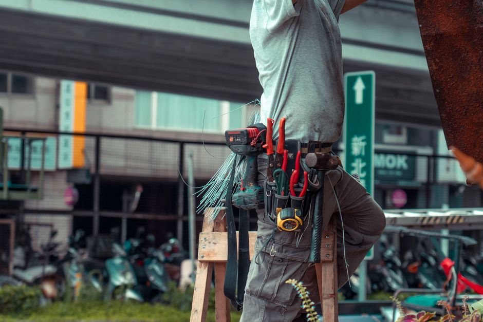 hidden costs of selling a home — Handyman standing on a ladder with tool belt, repairing outdoors with visible tools