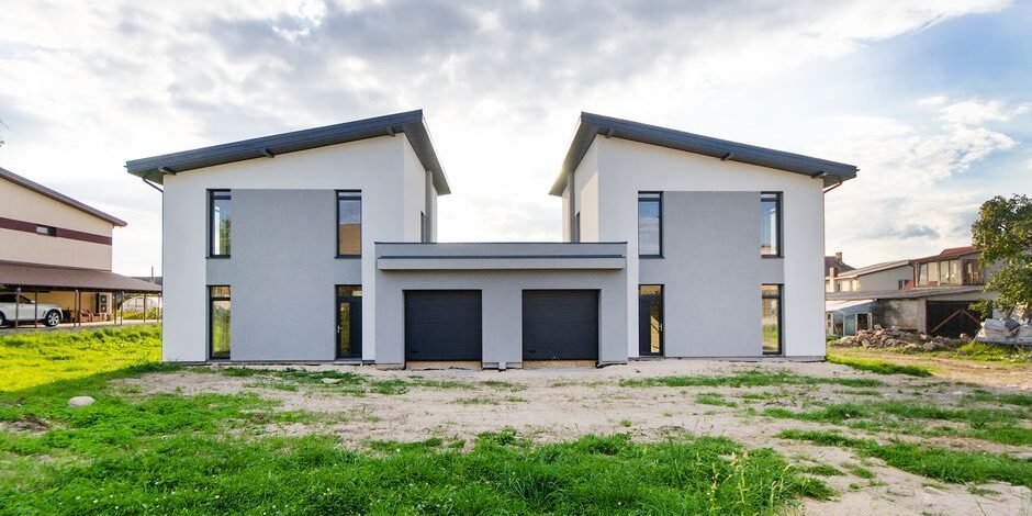 Front view of twin modern houses with a symmetrical architectural design under a cloudy sky. Front view of twin modern houses with a symmetrical architectural design under a cloudy sky.