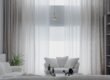 A minimalist living room with soft white sofas and large curtains, creating a cozy atmosphere