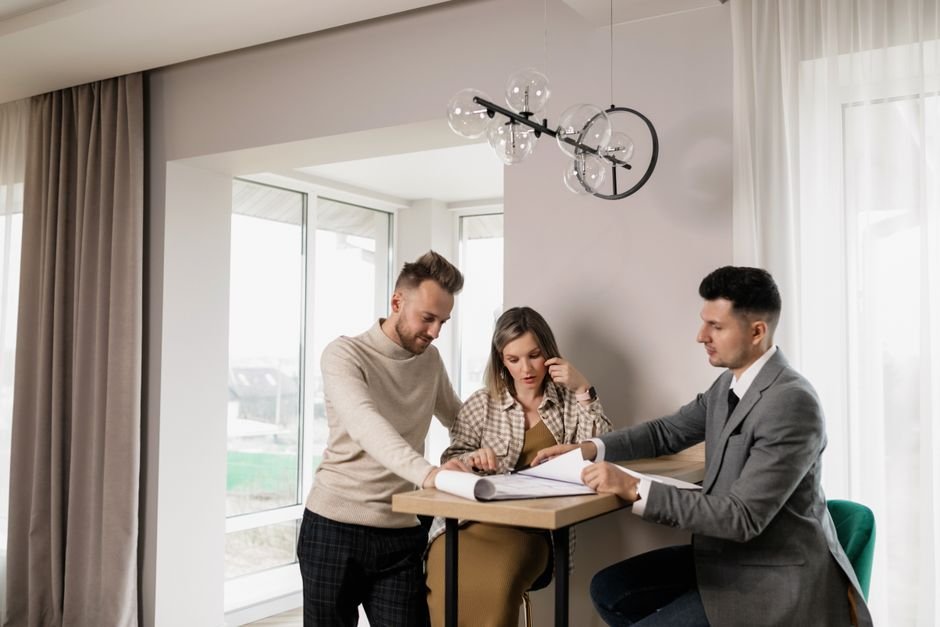 A couple consults with a real estate agent in a modern indoor setting, reviewing property documents